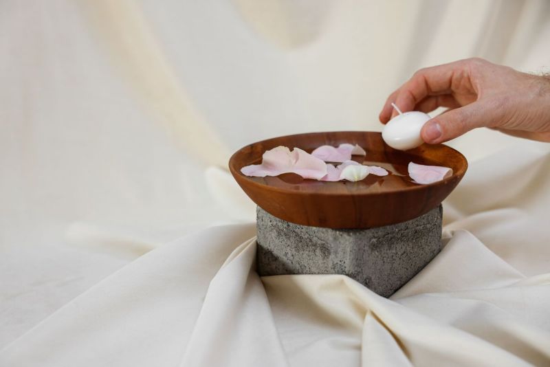Mano colocando una vela en un cuenco de madera con pétalos