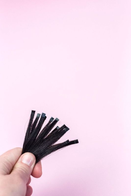 Dita che tengono sottili ciocche nere su sfondo rosa