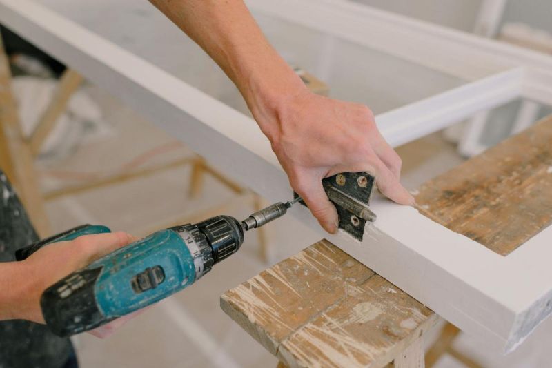 Manos atornillando una bisagra con un taladro en un marco de madera