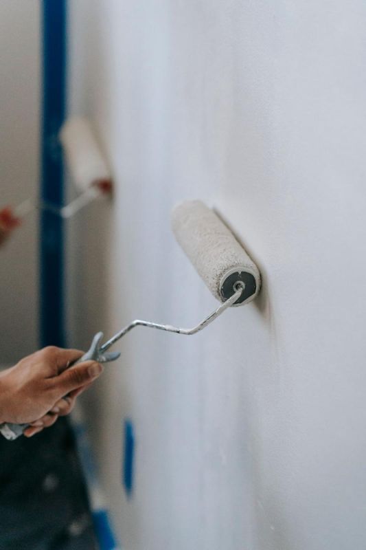 Hände streichen eine weiße Wand mit der Rolle