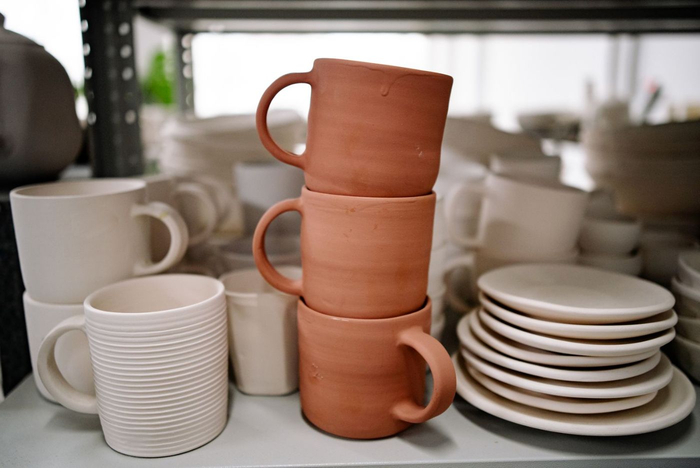 Tazas y platos de cerámica en tonos terracota sobre una estantería