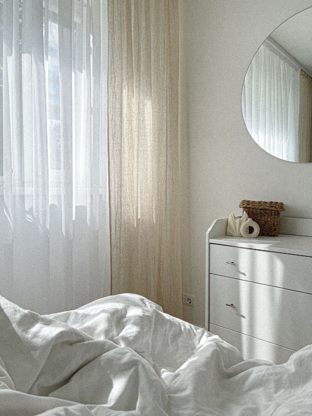 Cortinas de lino junto a un espejo redondo en una habitación luminosa