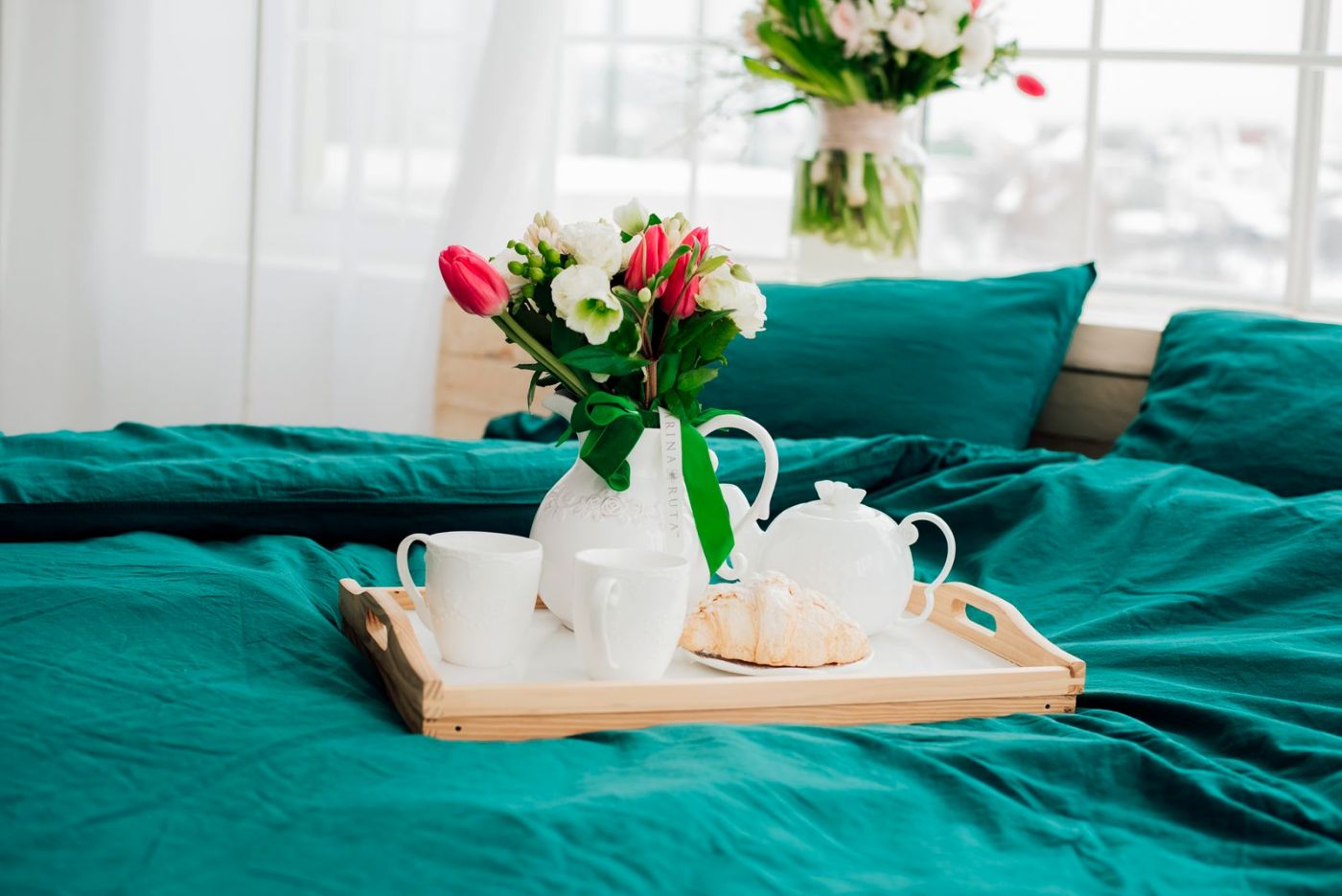 Cama con ropa verde y una bandeja con tulipanes y desayuno