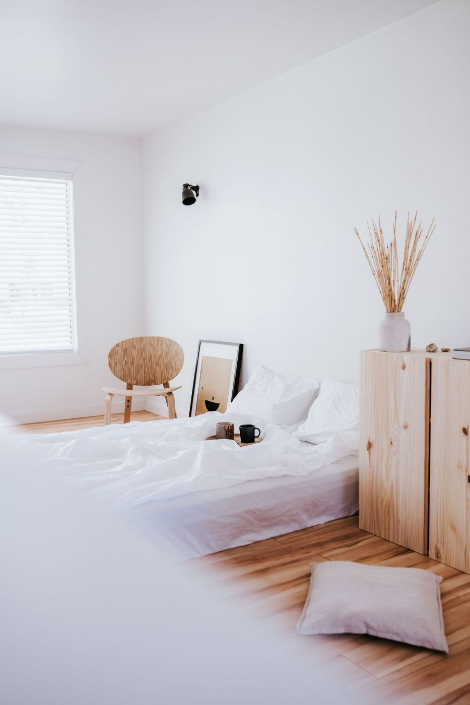 Dormitorio blanco y luminoso con una silla de madera y una ventana grande
