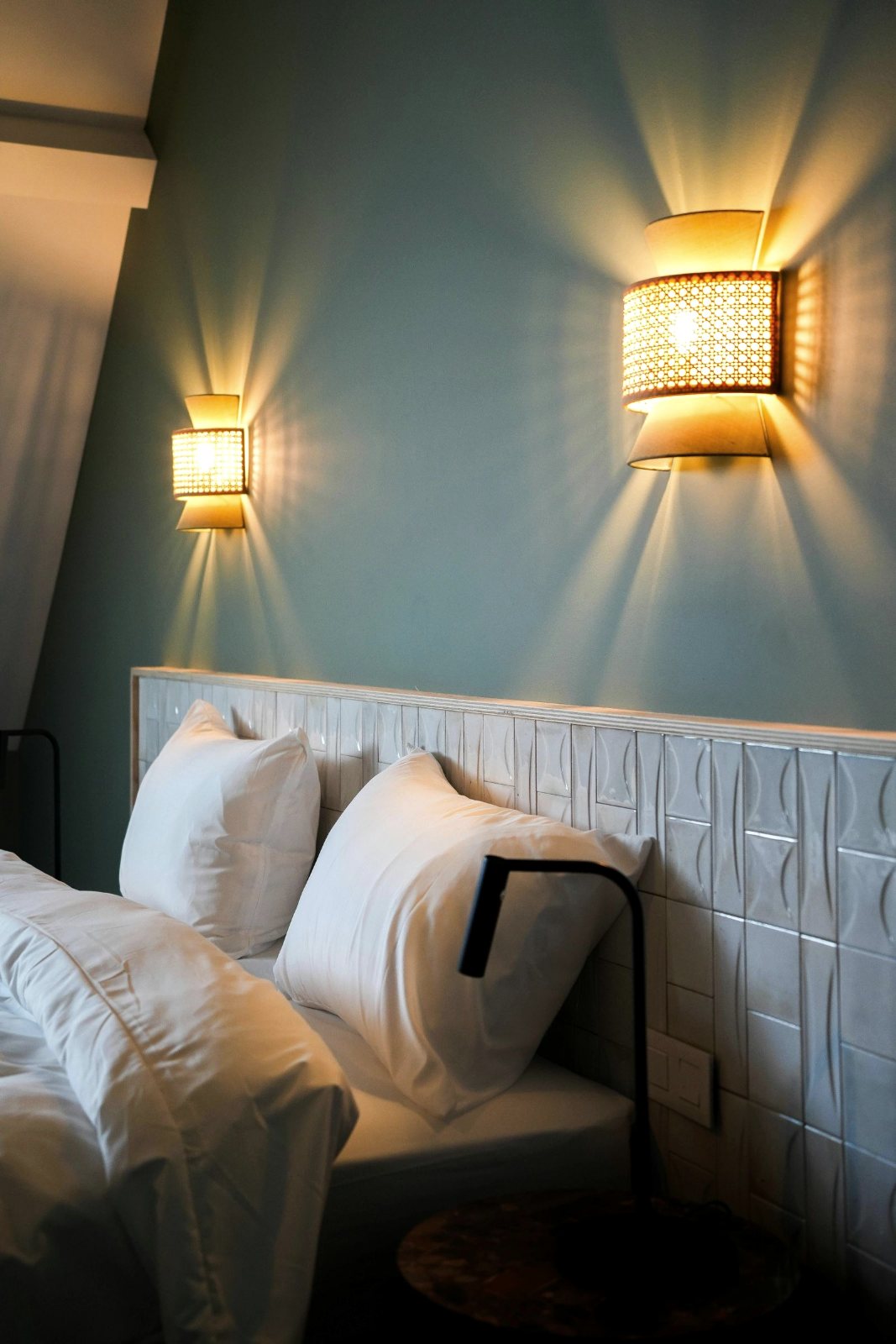 Cabecero blanco, pared verde y dos apliques de mimbre encendidos