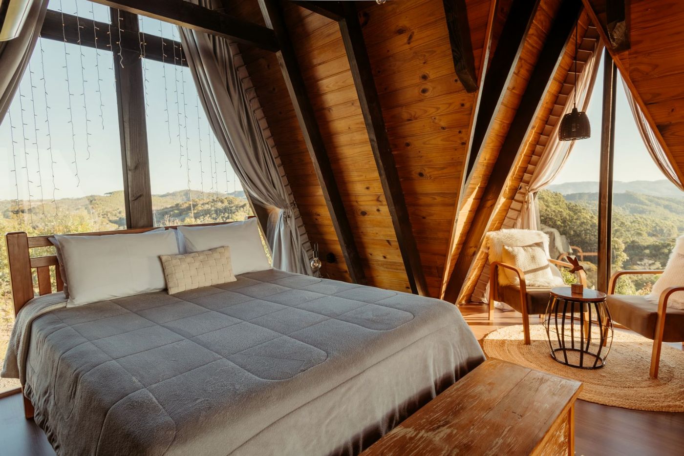 Cama doble bajo un techo de madera, con ventanal al valle