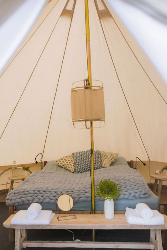Bed with cushions inside a canvas tent with a wicker lantern