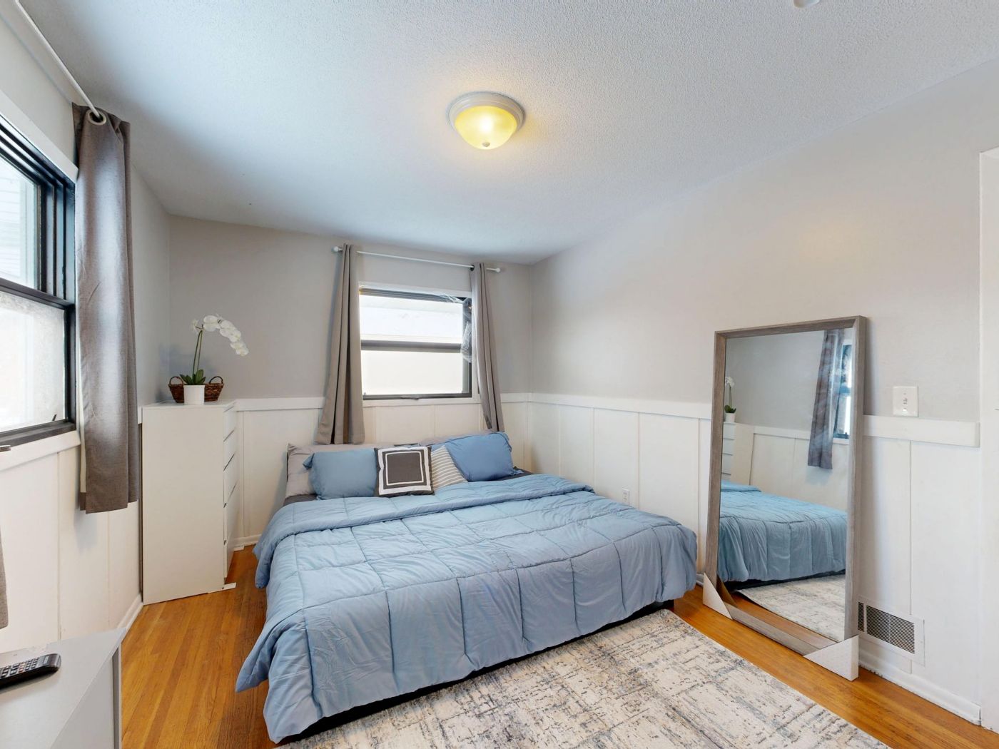 Habitación con cama doble de ropa azul, espejo y ventana