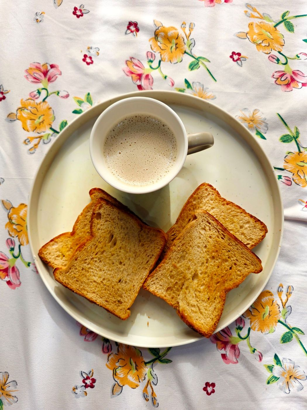 Plato con tostadas y una taza de café sobre un mantel de flores