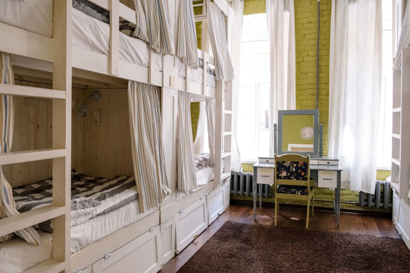 Dormitorio luminoso con literas con cortina y un tocador con silla