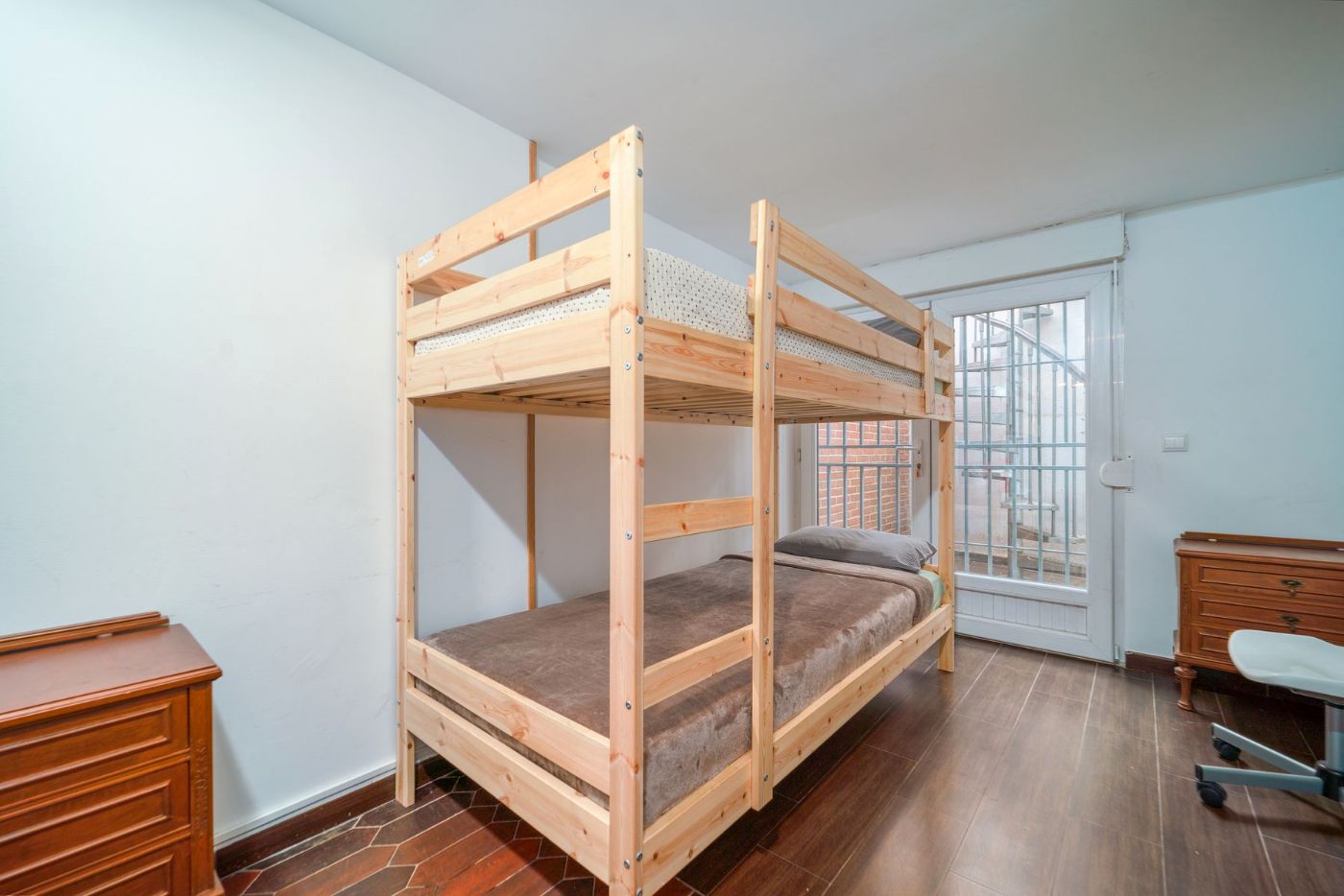 Litera de madera clara en una habitación con ventana y cómoda