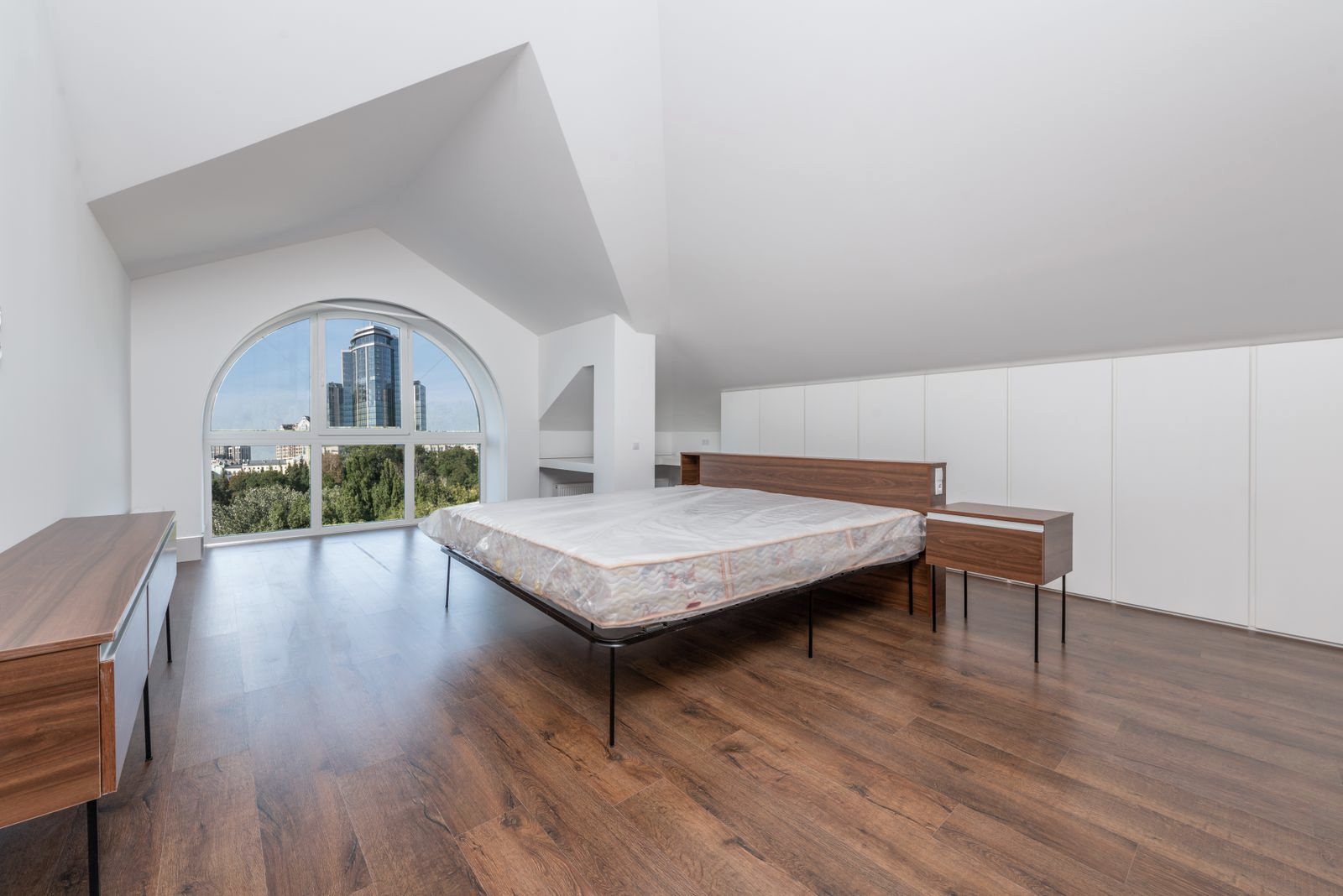 Loft con suelo de madera, cama grande y ventana en arco