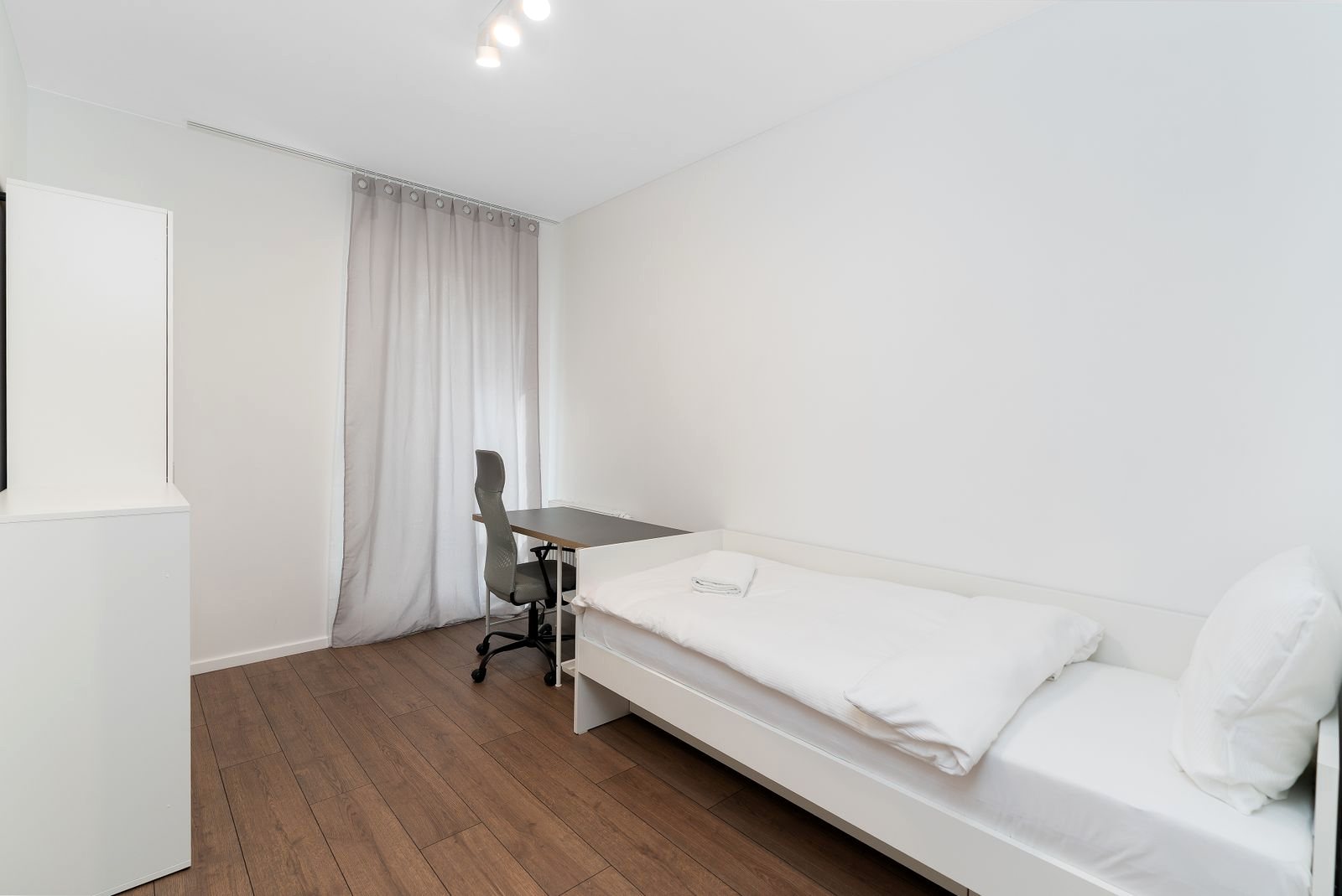 Habitación blanca con escritorio, silla y cama individual