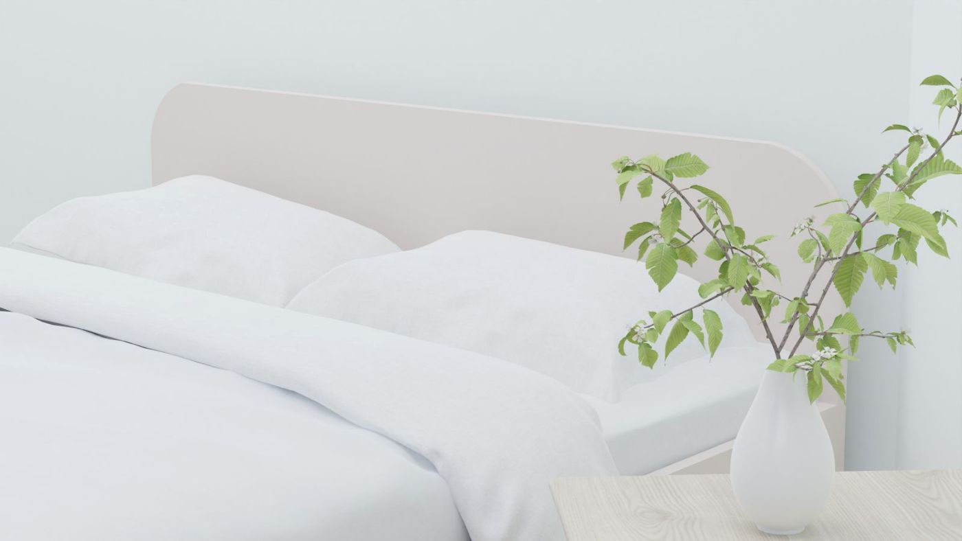 Cama con ropa blanca y una rama verde en un jarrón