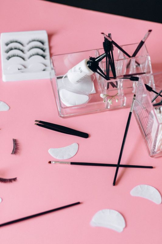 Herramientas de cejas y pestañas, trazos de cejas y una tira de pestañas sobre papel y fondo rosa