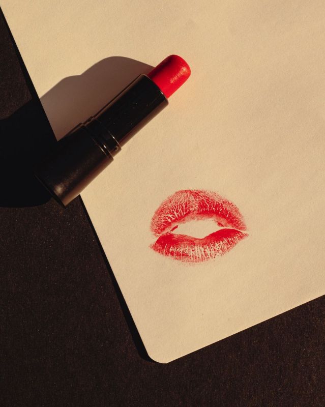 Impronta di labbra rosse su carta accanto a un rossetto