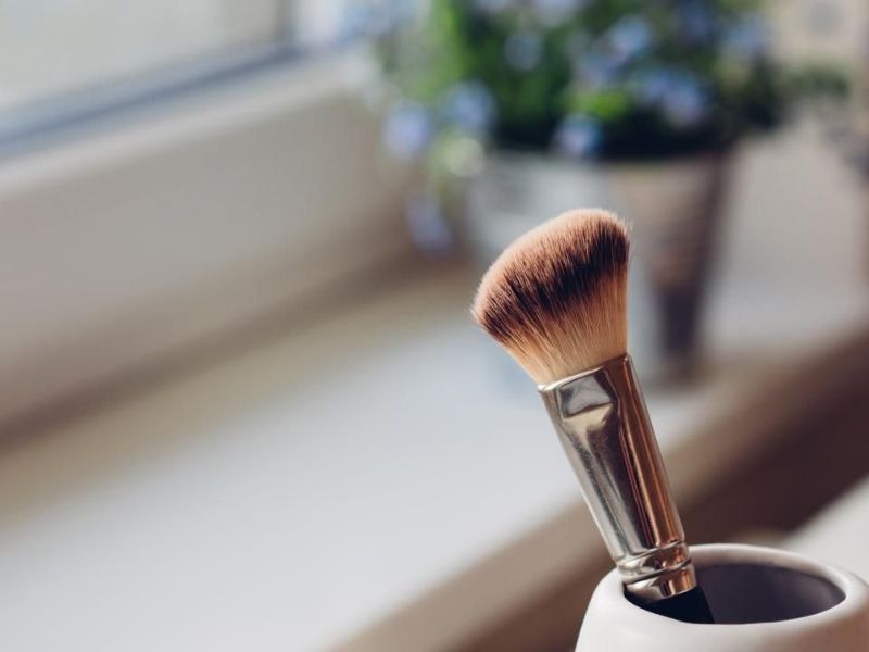 Un pinceau de maquillage dans un verre près d’une fenêtre lumineuse