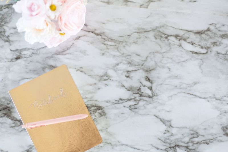 A golden notebook and flowers on white marble