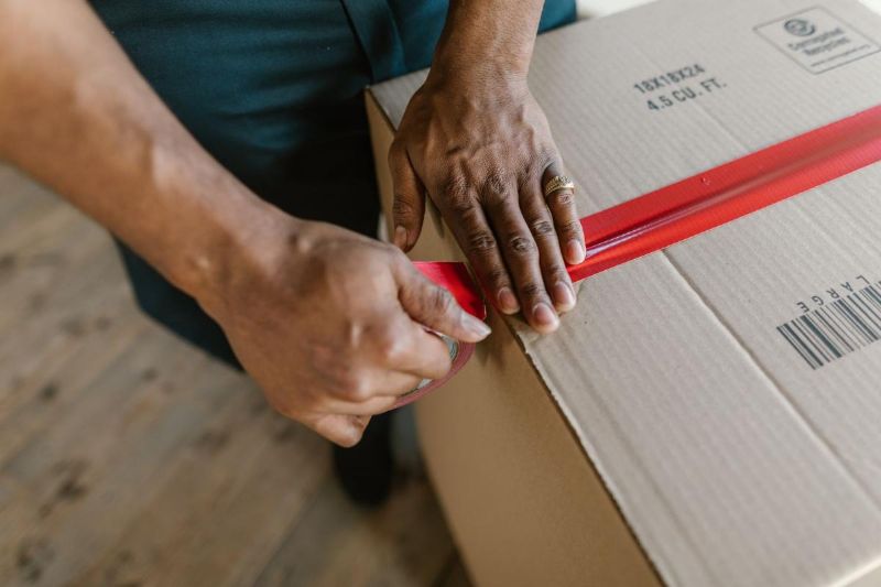 Hands closing a cardboard box with red tape