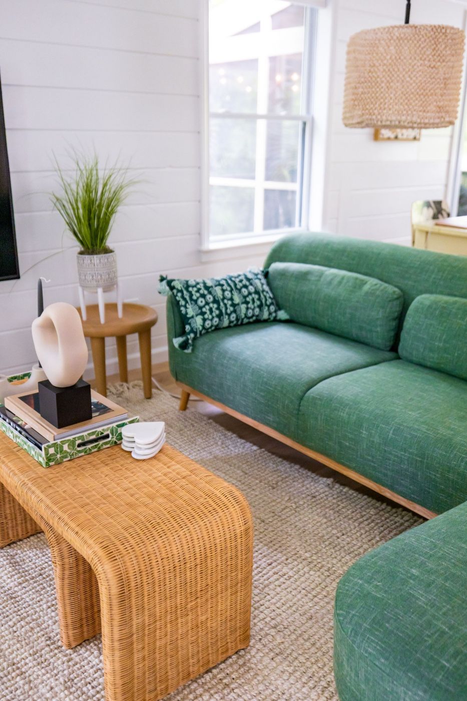 Salón con sofá verde, mesa de ratán y paredes claras