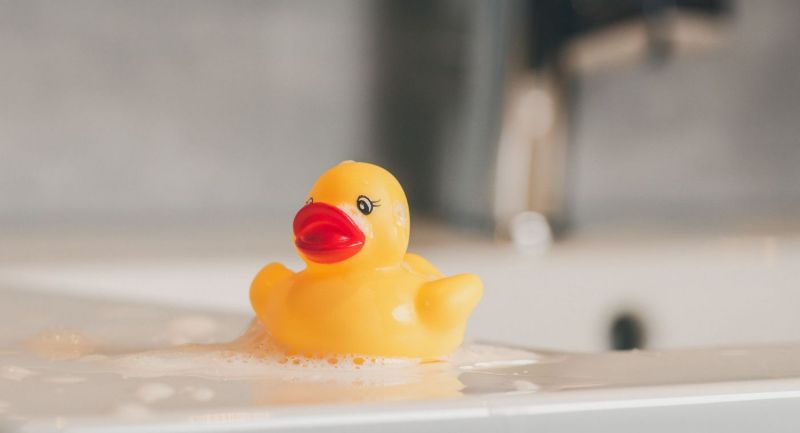 Patito de goma amarillo entre espuma en una bañera blanca