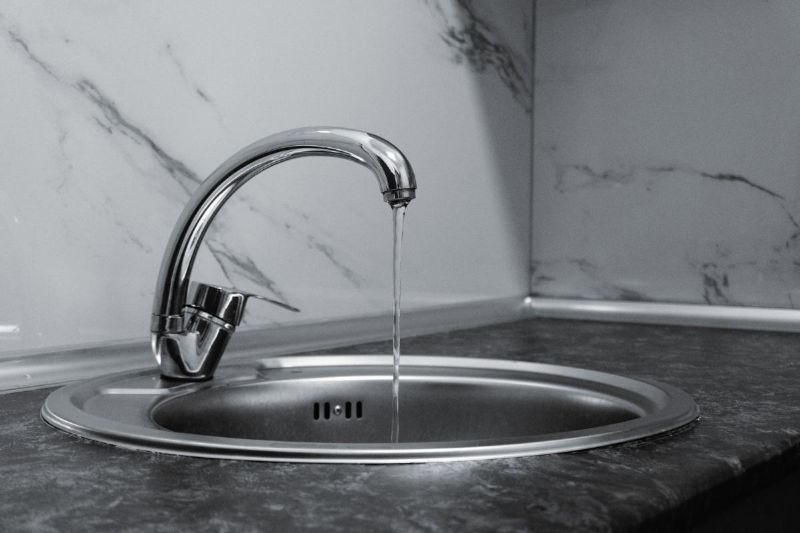 Grifo cromado con agua sobre encimera de mármol