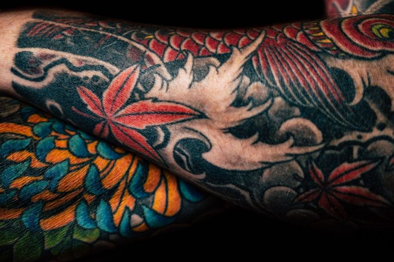 Avambracci con tatuaggi di stile tradizionale a colori: foglie rosse e onde